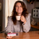 Jeune femme rousse buvant un café avec une boîte de compléments alimentaires antistress naturels puissants de la marque charlidéliss, le meilleur chocolat noir pour régime 